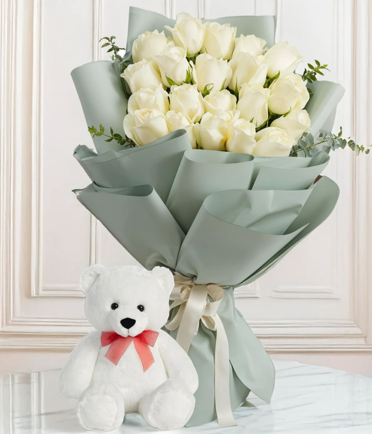 Teddy & Blooms Harmony a bouquet of white roses with green foliage wrapped in grey paper, accompanied by a white teddy bear with a red ribbon bow on its neck – Petal Frost flower shop